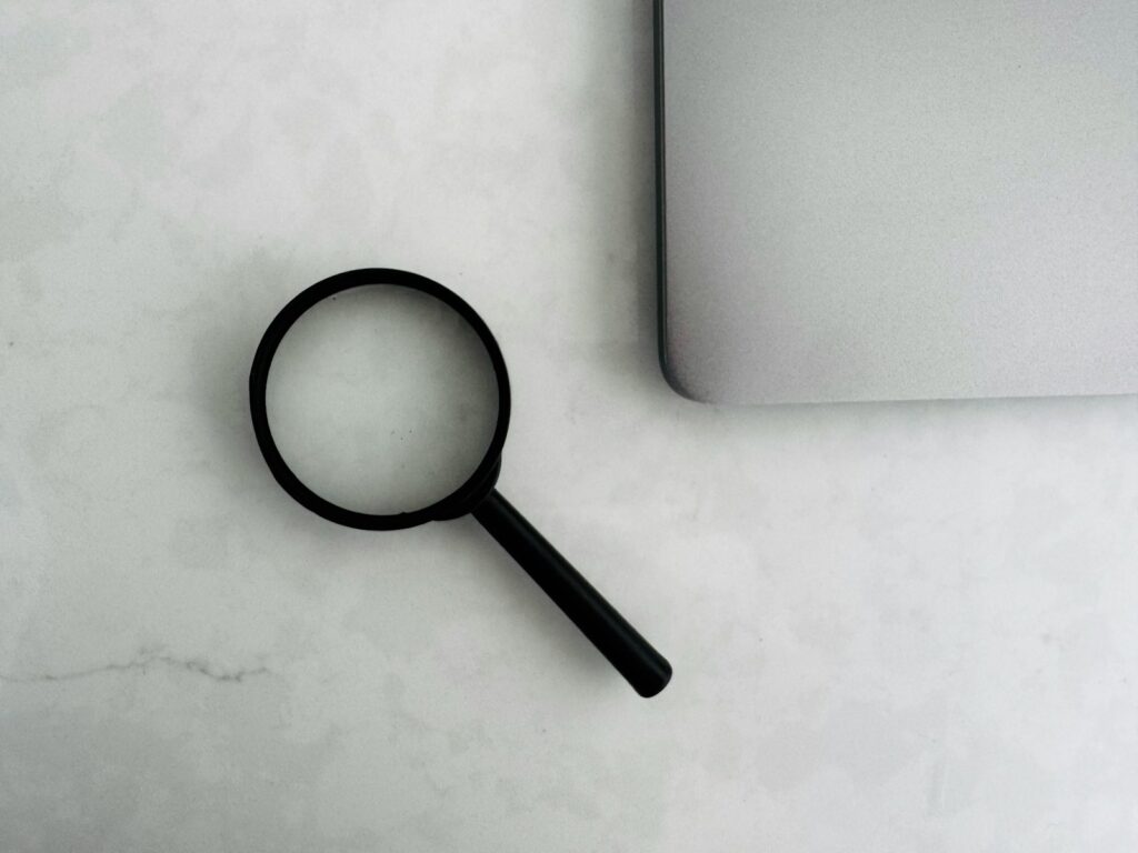 Generative Engine Optimization: Lupe neben Laptop als Symbol für Recherche in der KI-Suche