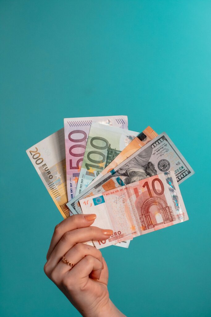 Währungsrisiken: Hand hält Euro- und US-Dollar-Banknoten als Fächer vor türkisem Hintergrund