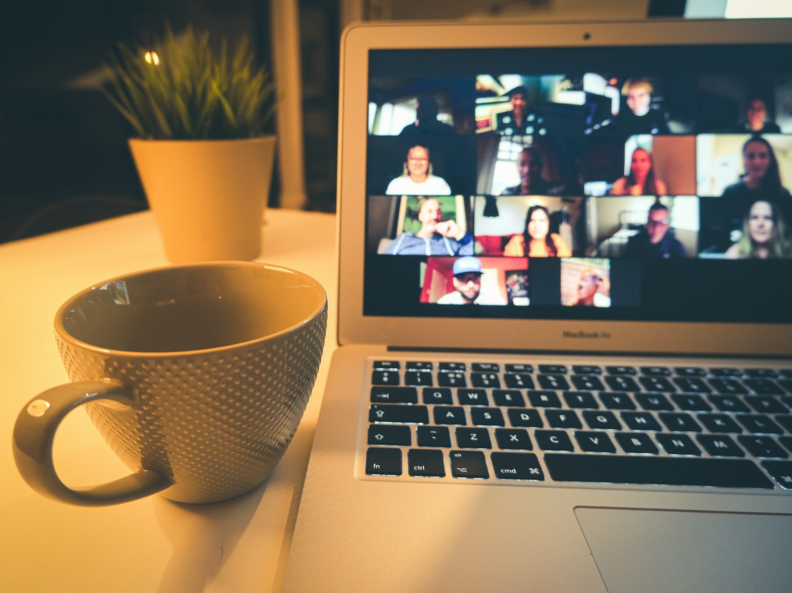 Deepfake-Betrug im Videocall: Laptop zeigt eine Videokonferenz mit vielen Teilnehmern, daneben eine Kaffeetasse