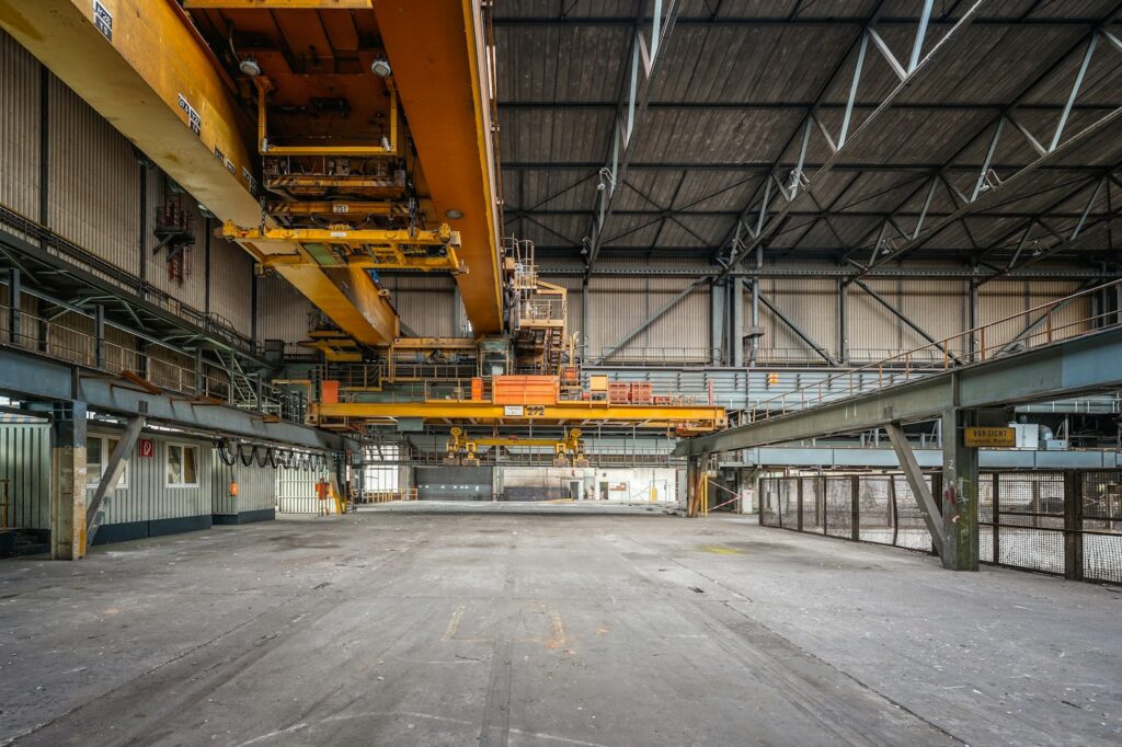 Deindustrialisierung sichtbar: leere Industriehalle mit gelben Deckenkränen und Betonboden