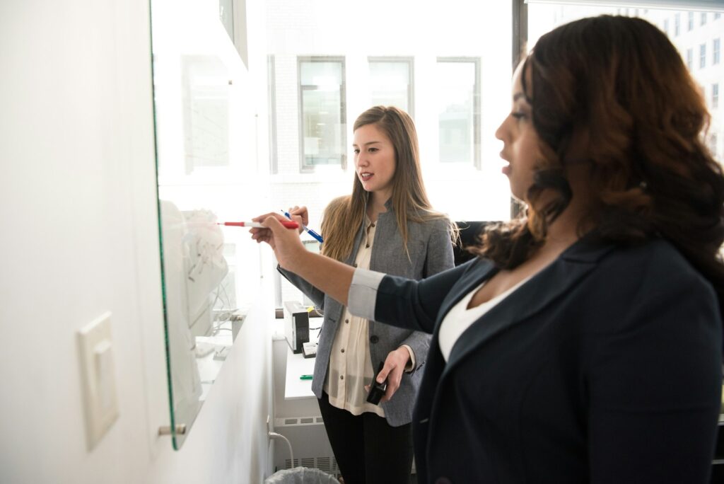 Entscheidungsfindung am Glasboard: Zwei Frauen sammeln Optionen und bewerten sie gemeinsam