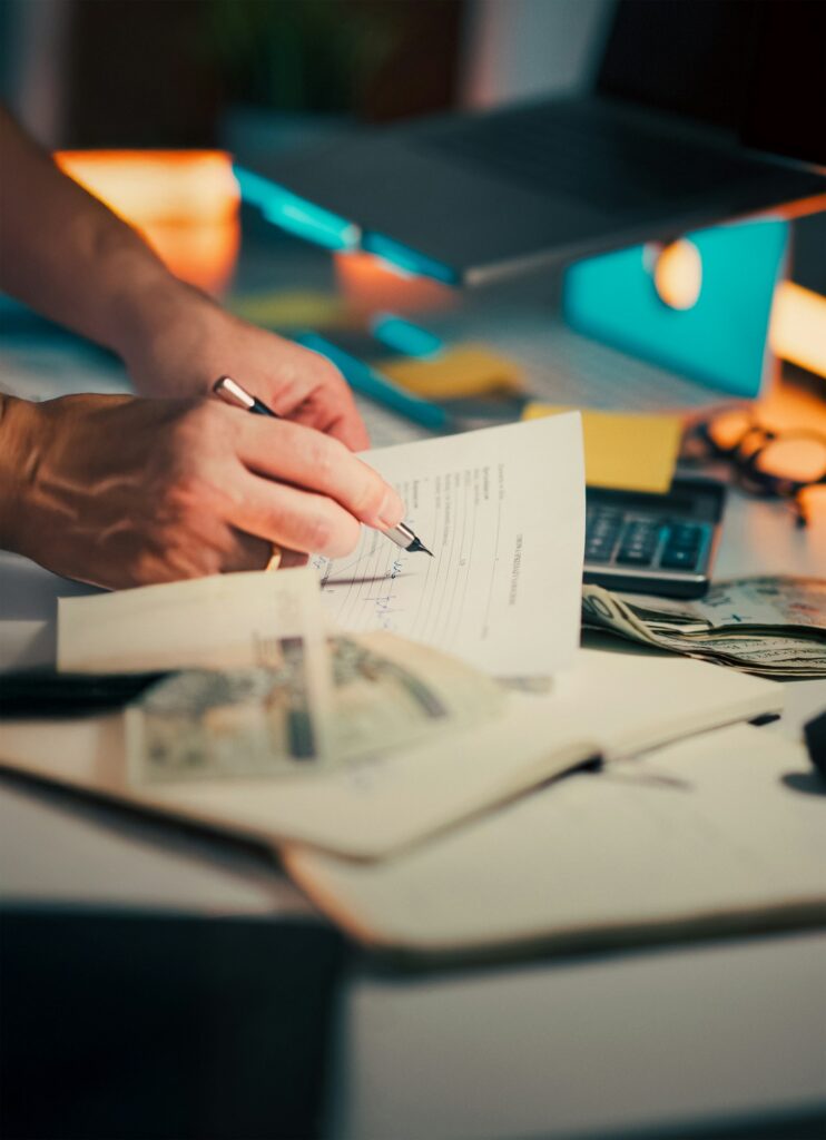 Factoring: Hand unterschreibt ein Dokument auf dem Schreibtisch neben Taschenrechner und Bargeld