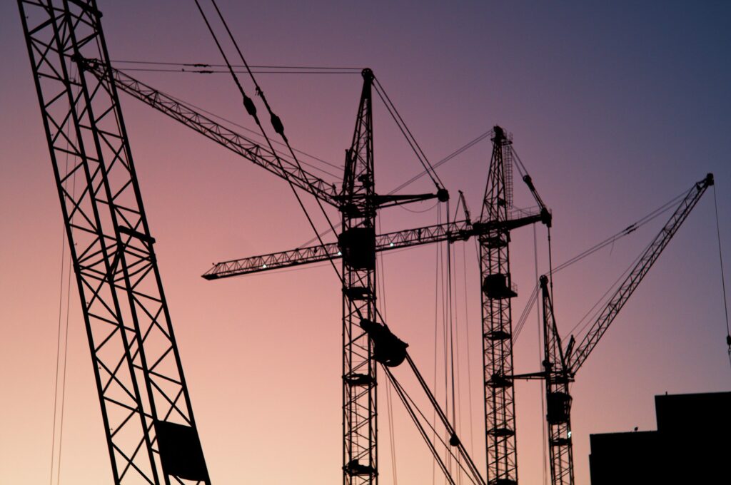 Firmeninsolvenzen im Baugewerbe: Mehrere Turmdrehkräne über einer Baustelle bei Sonnenaufgang