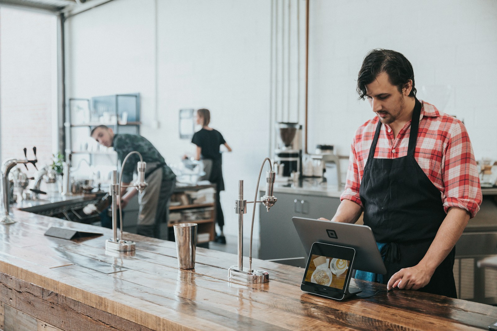 Mindestlohn 2027 in der Gastronomie: Barista bedient ein Tablet am Holztresen eines Cafés
