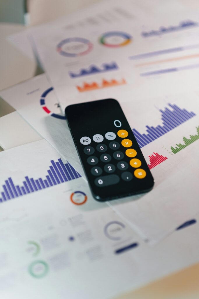 Mitarbeiterkosten berechnen: Smartphone mit Taschenrechner-App liegt auf Finanzberichten