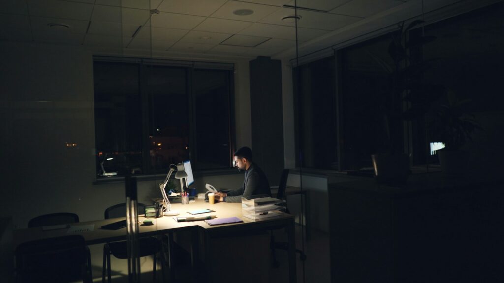 Schatten-KI im Büro: Mitarbeiter arbeitet spätabends allein am Computer in einem dunklen Büro